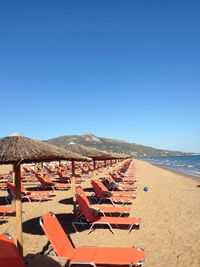 Empty deck chairs arranged at beach against clear blue sky