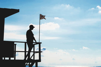 Silhouette man standing on lifeguard hut against sky
