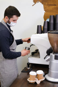 Barista serving coffee in takeaway cups in coffee shop in protective mask. coffee to go during