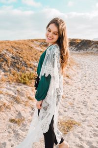 Side view of smiling young woman standing on sand at beach