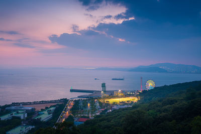 High angle view of illuminated buildings by sea against sky