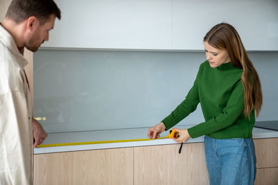 Man woman measuring surface on kitchen cabinets using measuring tape to buy household appliances.
