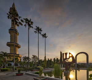 Palm trees in city against sky during sunset