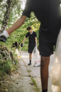 Teenage boys collecting plastic from plants in garbage bags on road