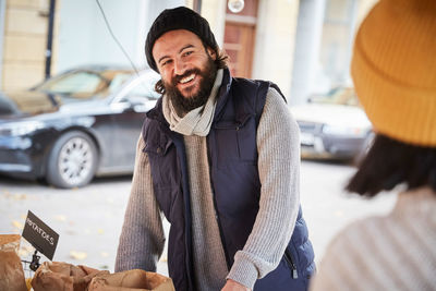 Smiling man looking at female vendor while standing by market stall