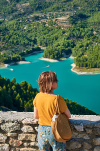 Rear view of man looking at lake against trees