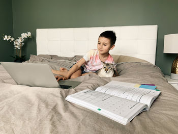 Boy child student with cat on bed. kid learning online on laptop. a new normal homeschooling.