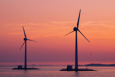 Wind turbines in sea against sky during sunset