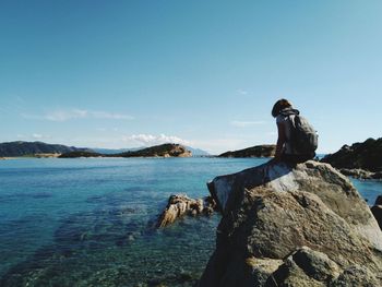 Woman sitting on rock at beach against blue sky