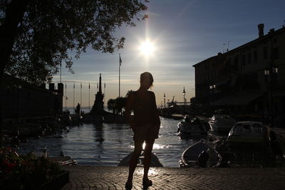 Rear view of woman standing on canal in city at sunset