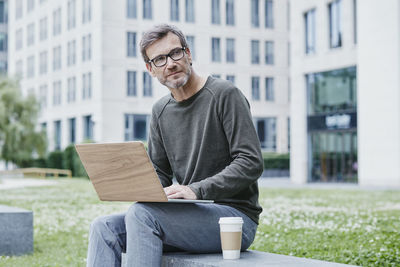Mature man outdoors with laptop and takeaway coffee