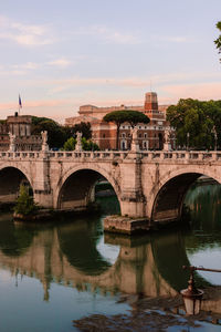 Arch bridge over river in city against sky