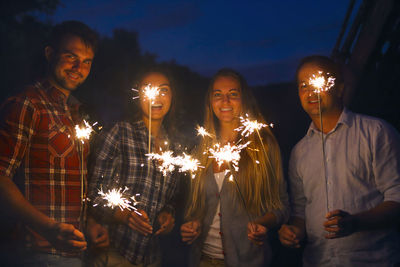 People holding sparklers against sky at night