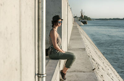 Full length of woman sitting on wall by river