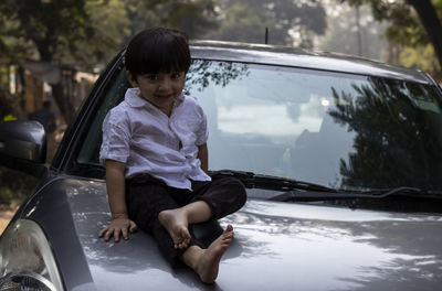 Indian cute baby boy sitting on car bonnet