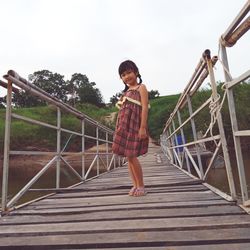 Portrait of girl standing on footbridge against clear sky