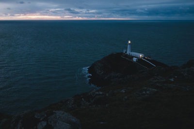 High angle view of illuminated lighthouse by sea against cloudy sky during sunset