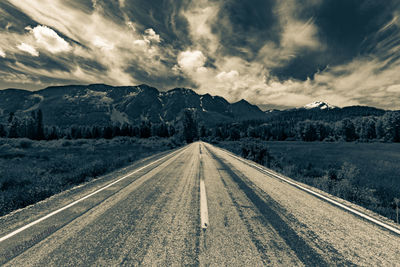 Empty road amidst grassy landscape against dramatic sky