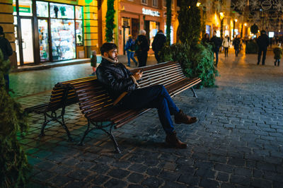 People sitting on bench at sidewalk cafe at night