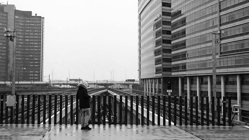 Rear view of person standing on bridge against clear sky in city