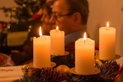 Close-up of burning candles over pine cones and ornaments with man in background