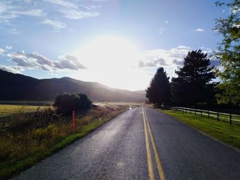 Empty road along trees and mountains against sky