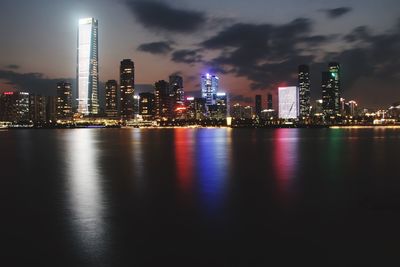 Illuminated buildings by river against sky at night