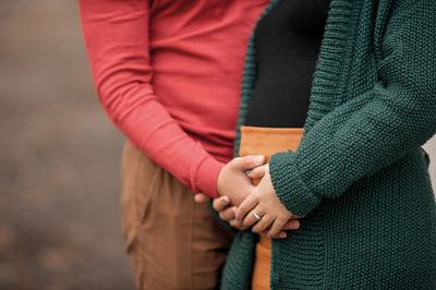 Man and woman hands hold pregnant woman tummy in atmosphere of autumn forest