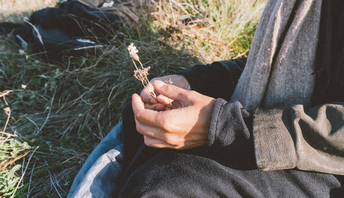 Midsection of man holding plant while sitting on grassy field