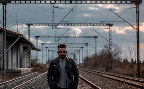 Portrait of man standing on railroad track against sky
