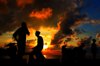 Silhouette people with motor scooter on pier against cloudy sky during sunset