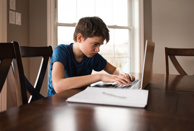 Tween boy working on his homework on a laptop commuter at home.