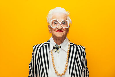 Portrait of stylish senior woman standing against yellow background