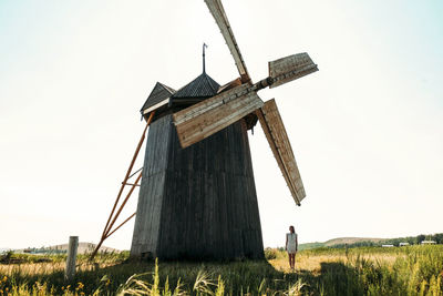 Woman standing by traditional windmill on field against clear sky