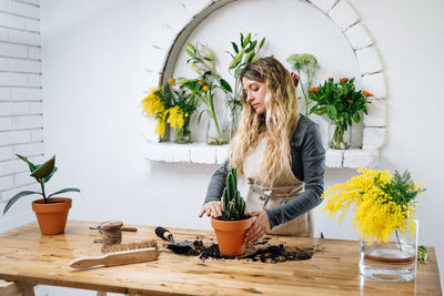 Woman holding flower pot on table by potted plant