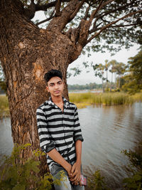 Portrait of man standing against tree trunk