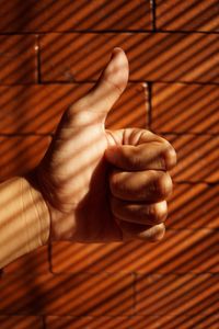 Close-up of hand showing thumbs up against brick wall