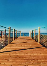Wooden pier on sea against clear blue sky