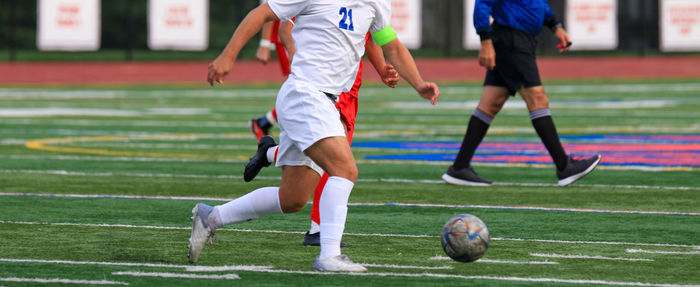 High school soccer player in a white uniform controlling the ball dribbling across the field.