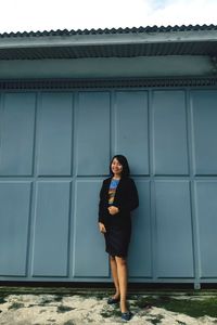 Portrait of young woman standing against building