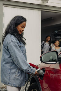 Side view of mature woman charging electric car outside house