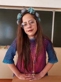 Portrait of confident student wearing wreath while standing against blackboard in classroom