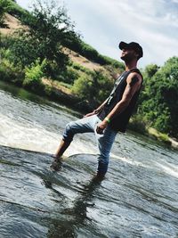 Side view of young man standing in lake against sky