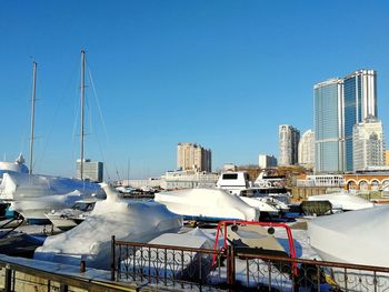 Boats moored at harbor by buildings against clear blue sky