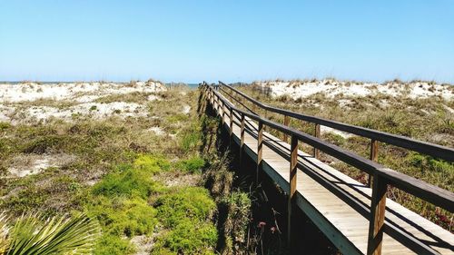 Footbridge over landscape against clear blue sky