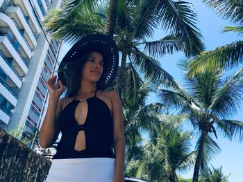 Low angle view of young woman standing on palm tree