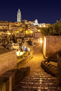 Illuminated street amidst buildings in town against sky at night
