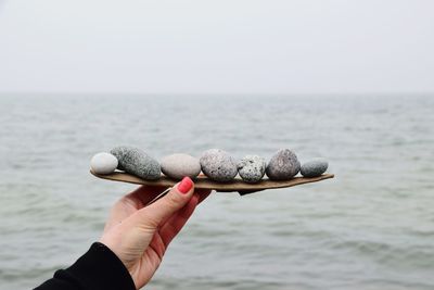 Close-up of hand holding stones against sea