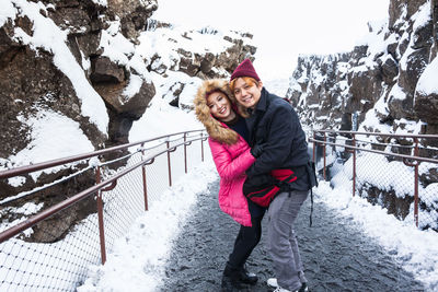 Portrait of smiling couple embracing while standing on road amidst mountain