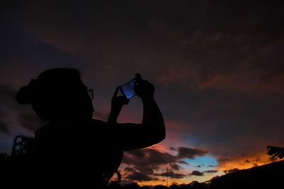 Rear view of woman photographing against sky during sunset